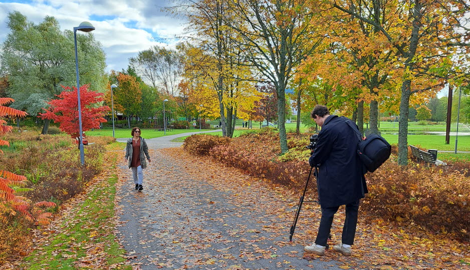 Kvinna går i park, en man filmar.